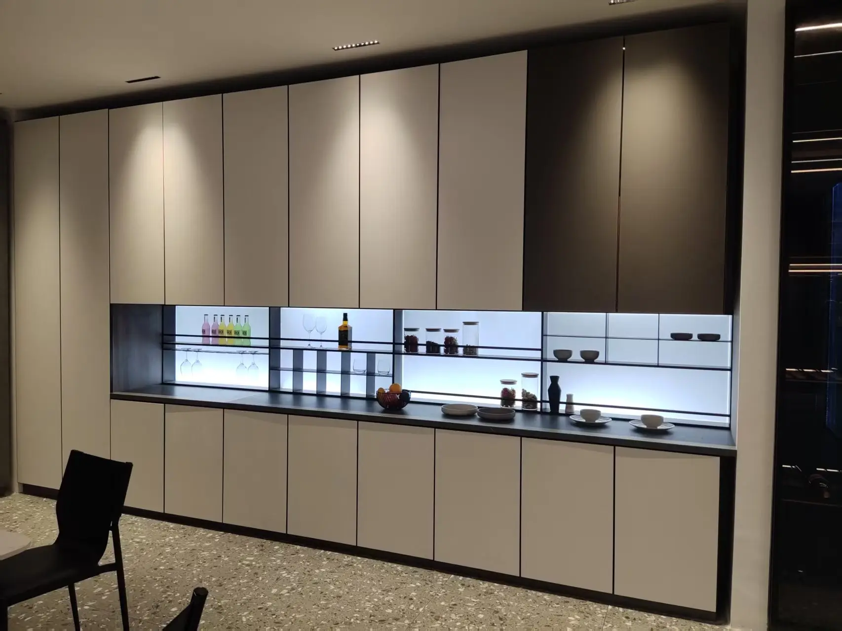 Full-height cabinet wall with a continuous illuminated glass display bay