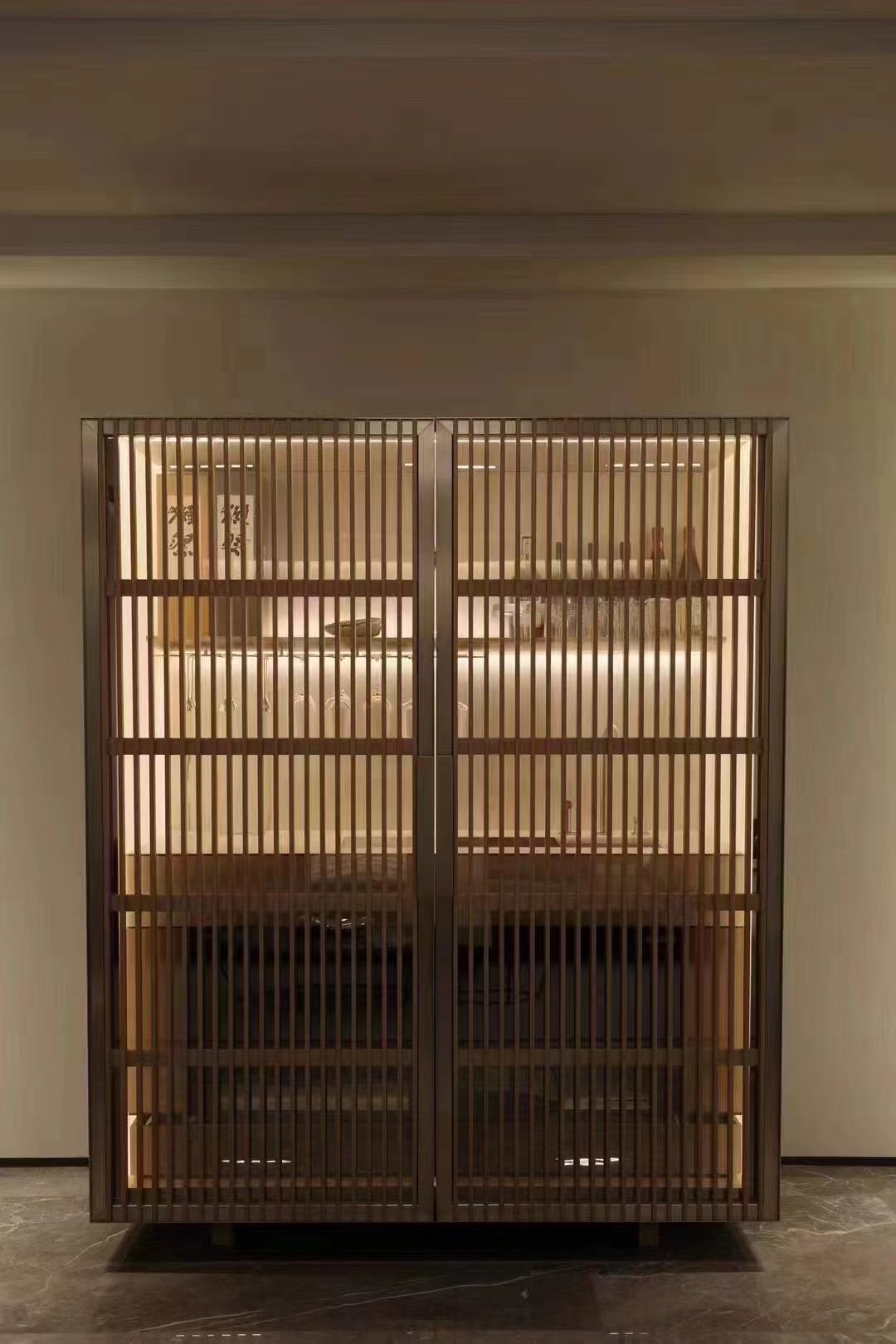 Tall illuminated glass cabinet behind vertical louvres